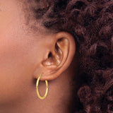 25 mm slim hoop earrings in solid 14K yellow gold shown on ear